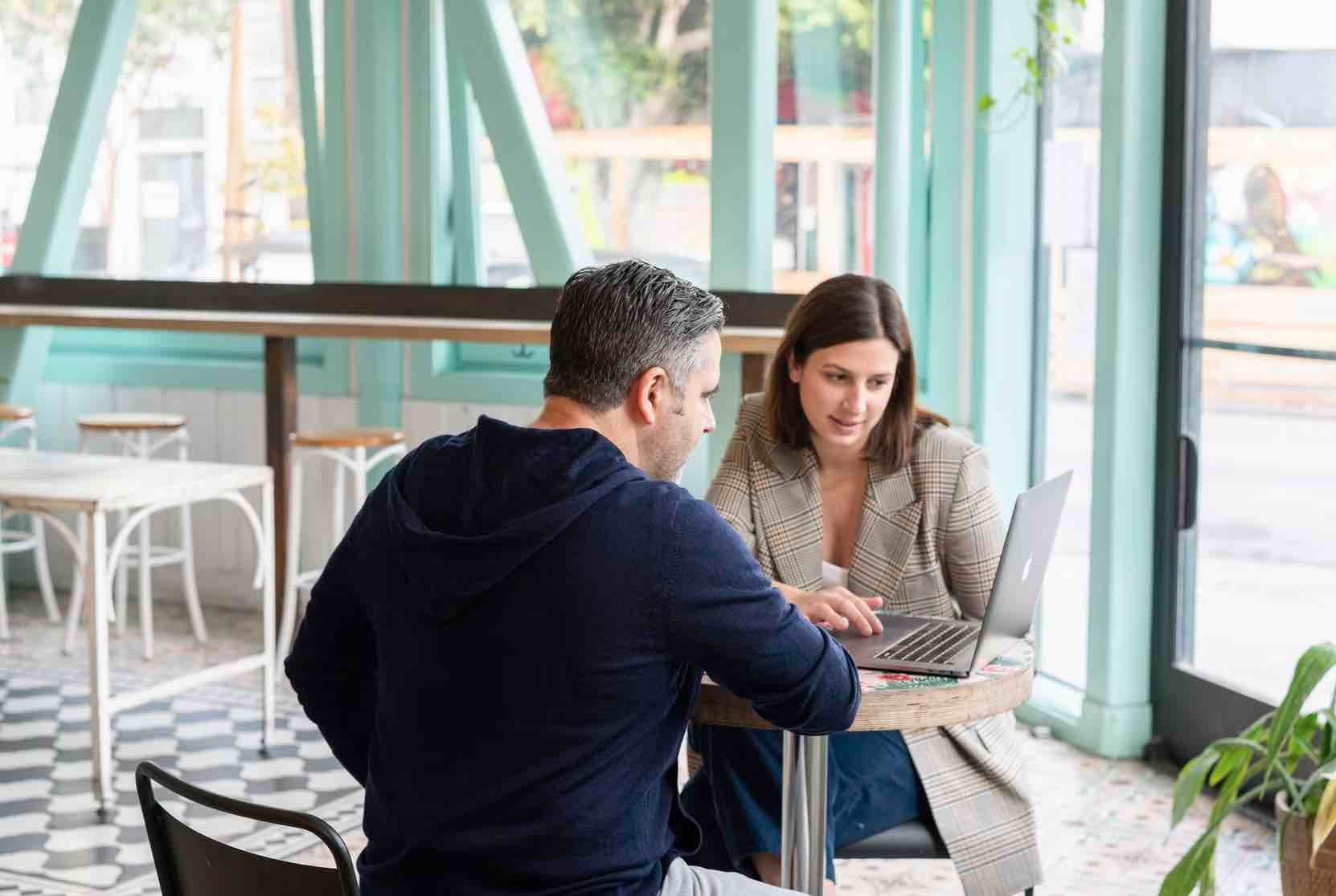 Zwei Personen arbeiten in einem Café gemeinsam am Laptop